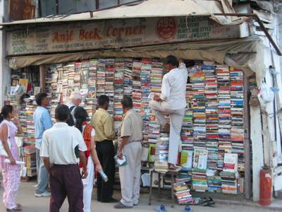 Straatboekwinkel met hoge stapels tweedehands boeken en klanten die bladeren en kopen.