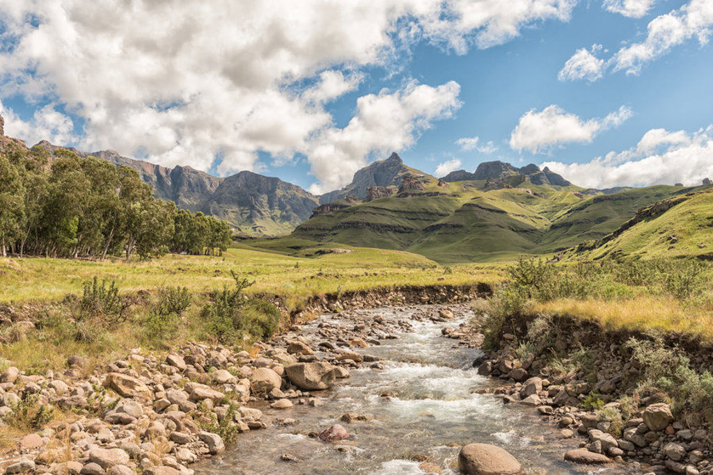 Groene bergvallei met kabbelende rivier in Noordelijk Zuid-Afrika, onder een blauwe lucht met wolken.