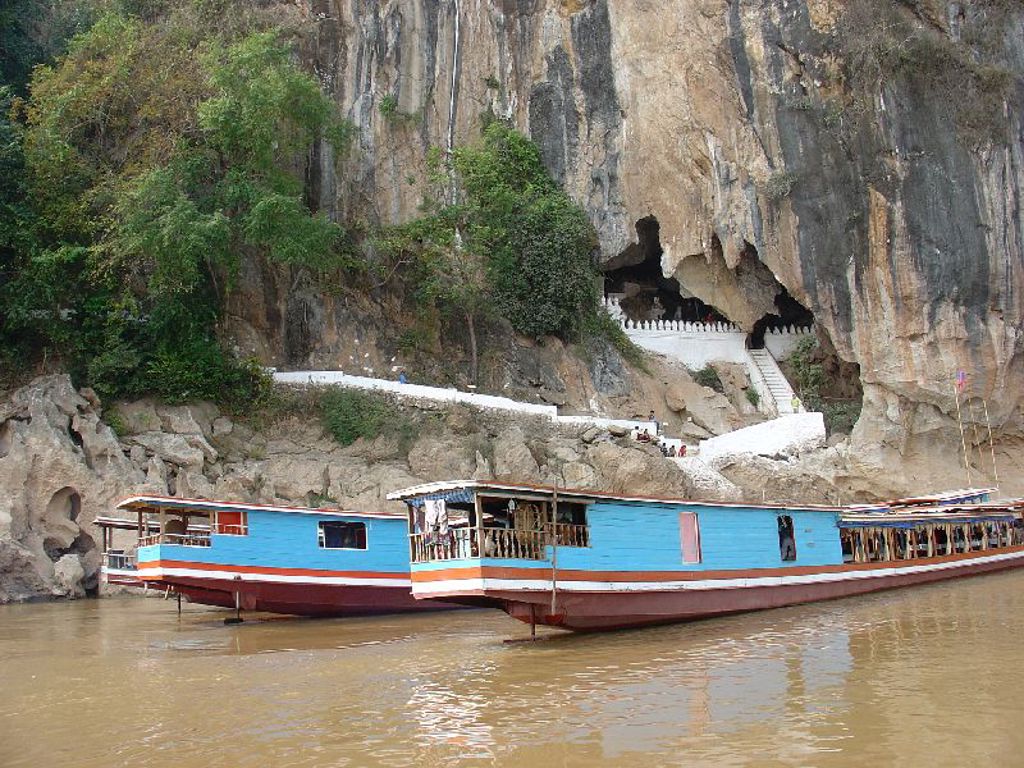 Rivierboot bij kalkstenen rotswand en grot, tijdens groepsrondreis Laos & Cambodja.
