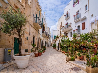 Sfeervol straatje in Puglia met witte huizen, balkons en bloempotten langs de route Alberobello–Matera.