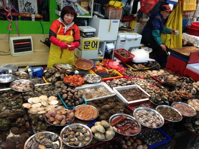 Visverkoper op een Zuid-Koreaanse vismarkt met verse schelpdieren, krab en octopus.