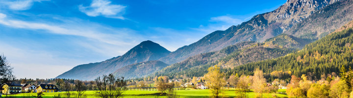 Berglandschap in Slovenië met groen dal, dorp en bossen onder een blauwe lucht.