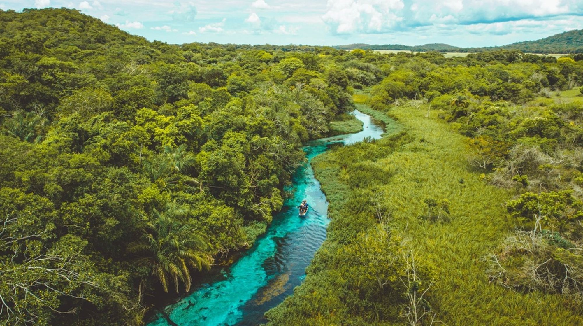 een turquoise rivier door het groene regenwoud in Brazilië, met een bootje op het water.