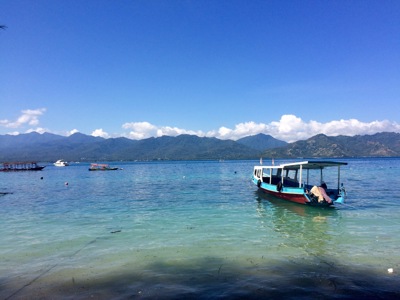 Boot op helderblauw water met uitzicht op bergen tijdens de Route Bali & Lombok.