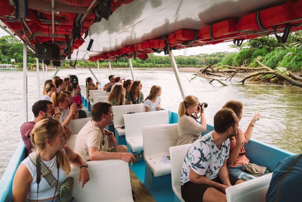 Groep 22-35ers op boottocht door de natuur in Costa Rica, speurend naar wildlife langs de rivier.