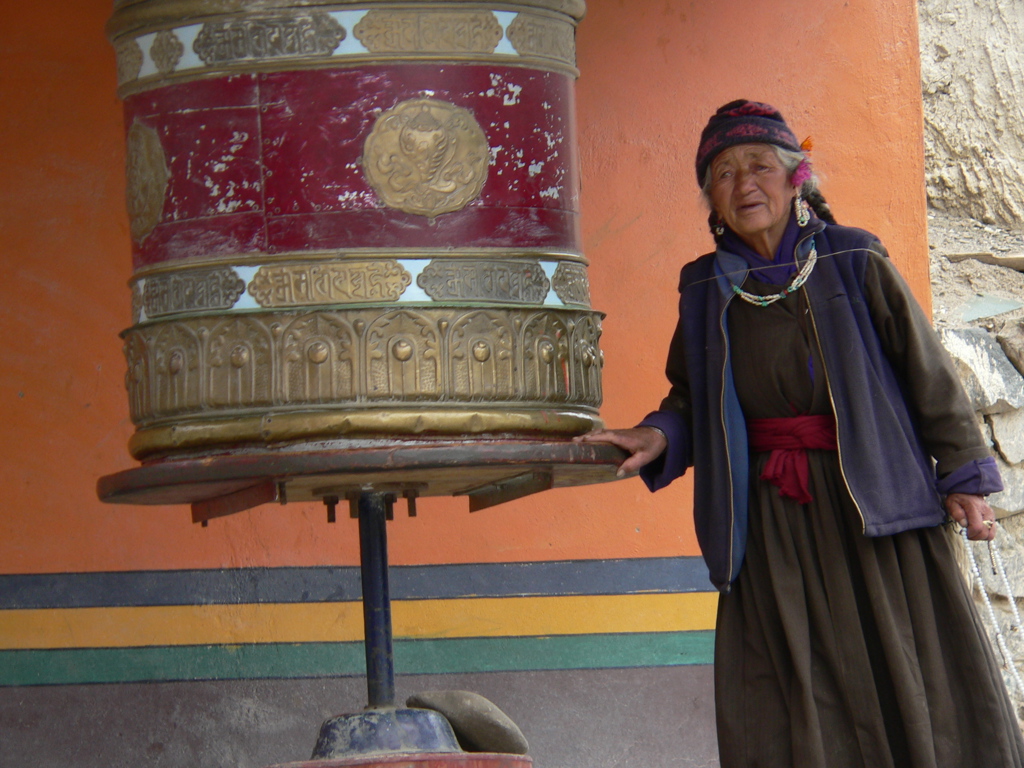 Vrouw bij groot gebedswiel bij een klooster in Ladakh, tijdens groepsrondreis India Spiti & Ladakh.
