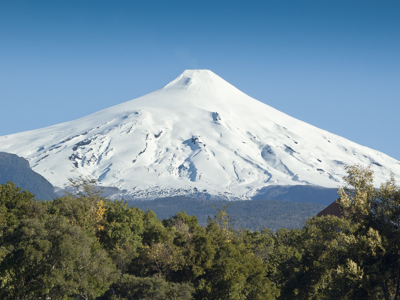 Sneeuwbedekte vulkaan Osorno in Patagonië, met groen bos op de voorgrond en blauwe lucht.