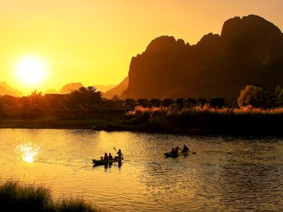Zonsondergang boven de Nam Song-rivier bij Vang Vieng, met kajakkers en karstbergen in Laos.