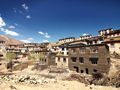 Traditioneel bergdorp in Spiti & Ladakh met lemen huizen tegen de helling onder een heldere blauwe lucht.
