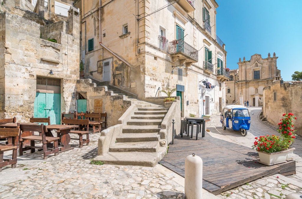 Historisch straatje in Matera, Puglia, met stenen trappen en een blauwe driewieler.