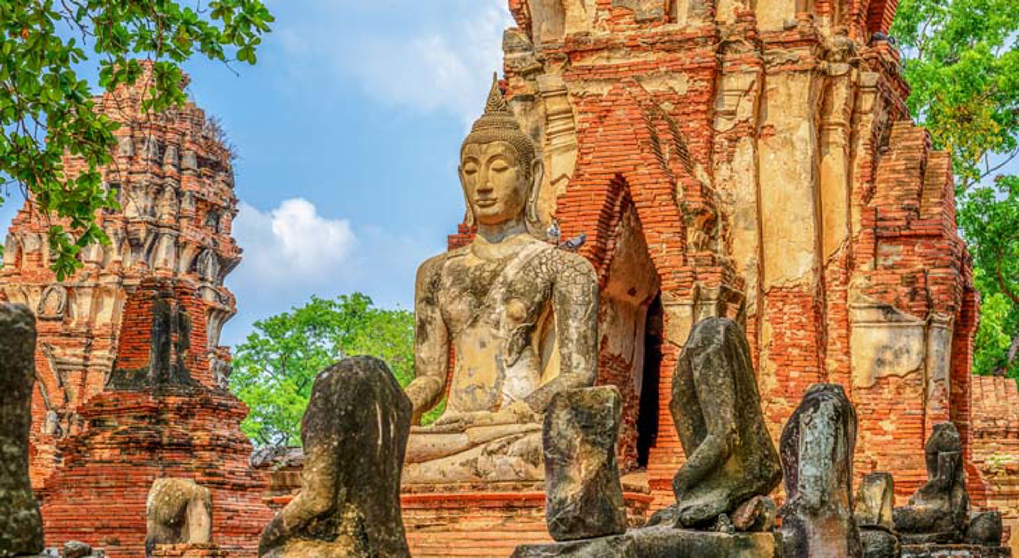 Wat Mahathat tempel Ayutthaya Thaise tempelruïne met stenen Boeddhabeeld tussen bomen.