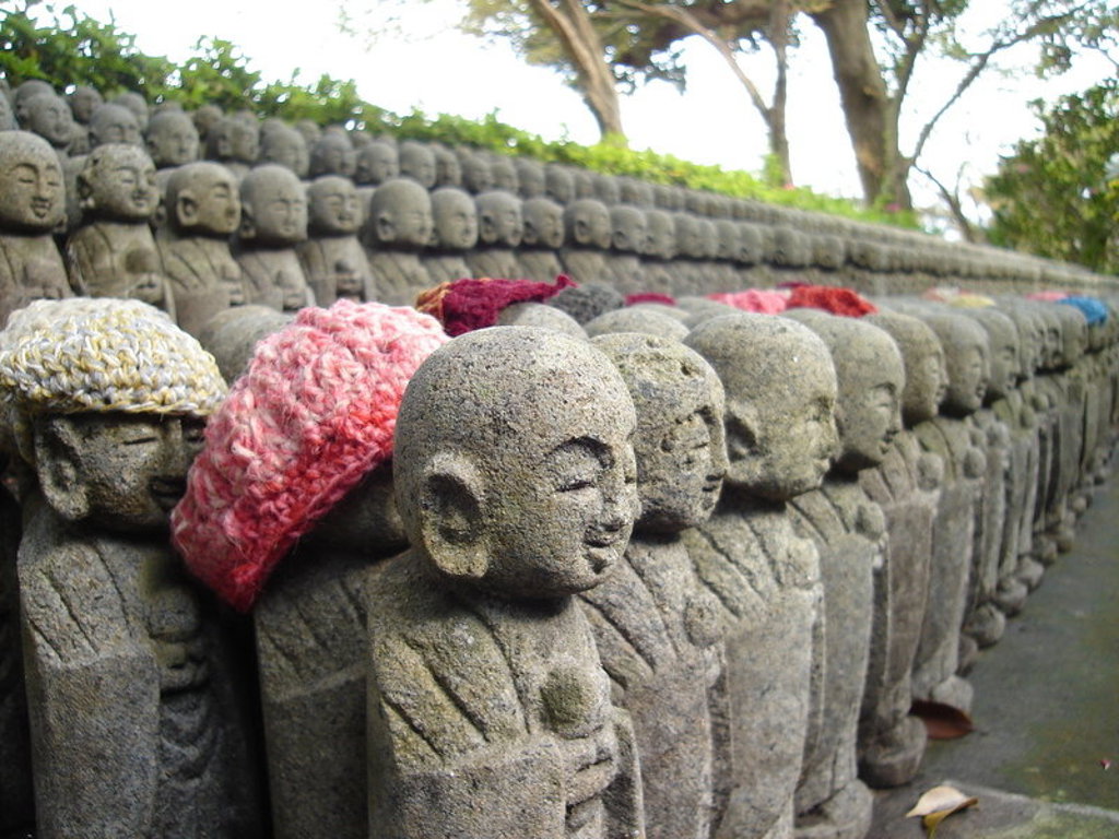 Rij Jizo-beeldjes met gebreide mutsen bij een tempel in Japan tijdens een groepsrondreis langs hoogtepunten.