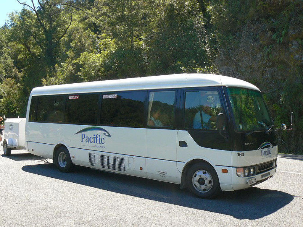 Tourbus tijdens groepsrondreis Nieuw-Zeeland, rijdend langs groene natuur in de bergen.