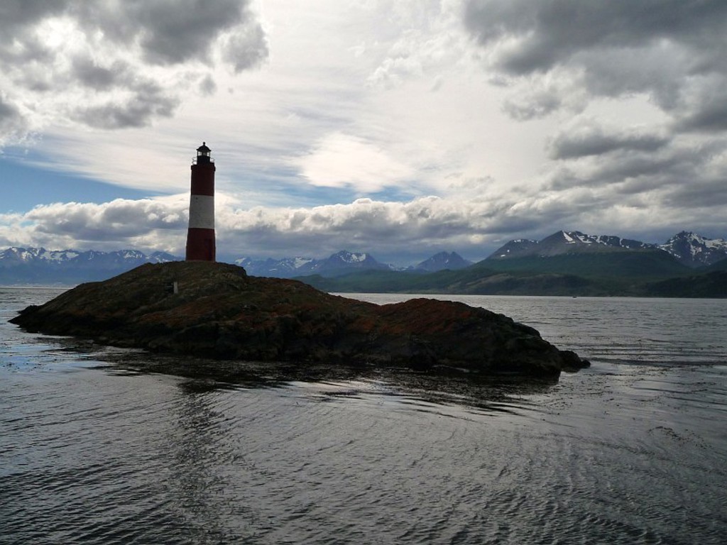 Vuurtoren op rotsachtig eiland met besneeuwde bergtoppen aan de horizon tijdens een groepsrondreis Patagonië.