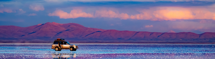 4x4 op de zoutvlakte Salar de Uyuni in Bolivia, met reflecties en bergen bij zonsondergang.