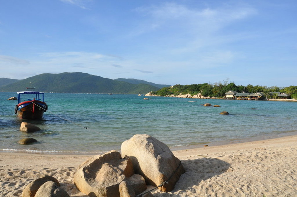 Strand in Vietnam met vissersboot op turquoise zee en groene heuvels op de achtergrond.