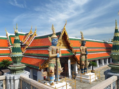 Wat Arun-tempelcomplex in Bangkok met kleurrijke daken en wachtersbeelden onder een blauwe lucht.