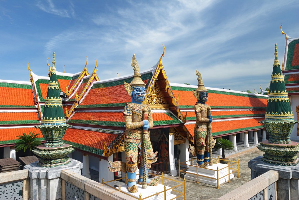 Wat Arun-tempelcomplex in Bangkok met kleurrijke daken en wachtersbeelden onder een blauwe lucht.
