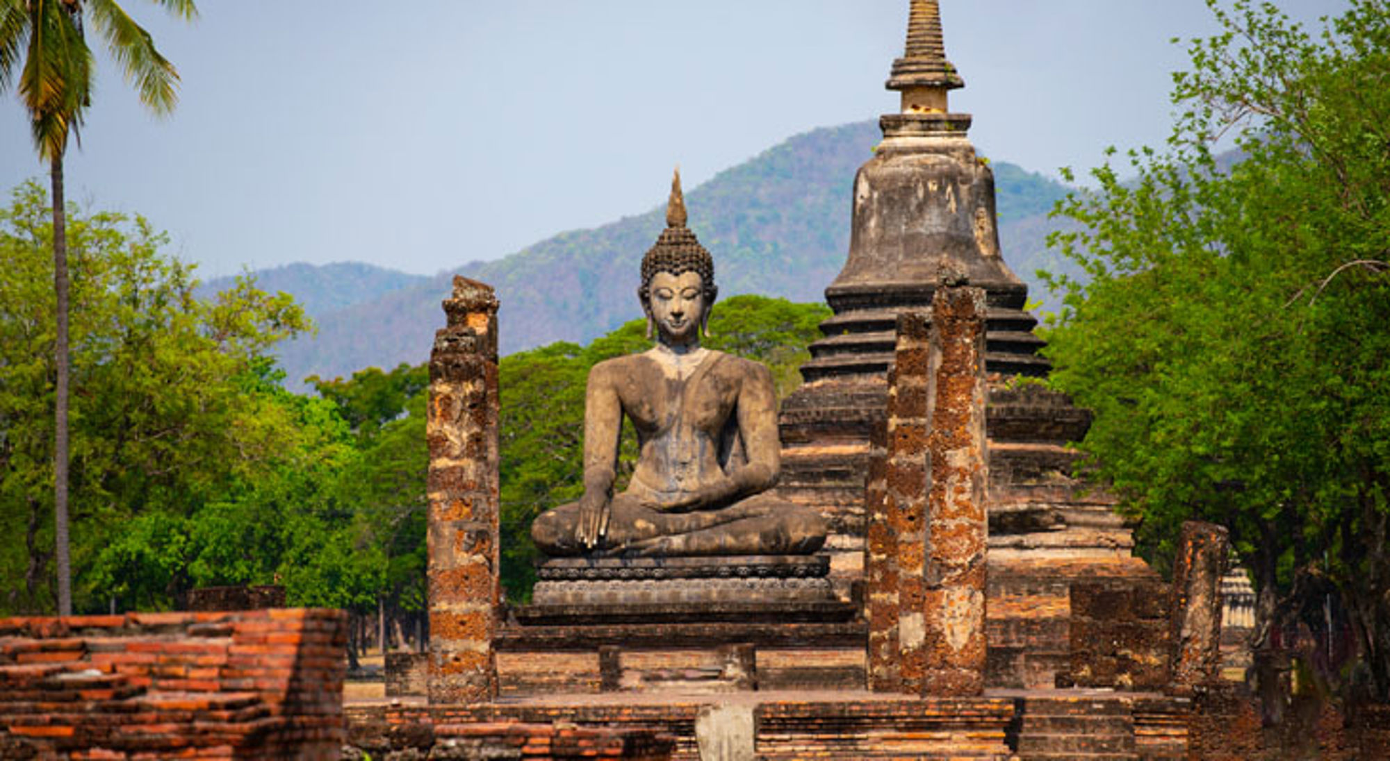 Boeddhabeeld bij oude tempelruïnes in Sukhothai Historical Park, Thailand.