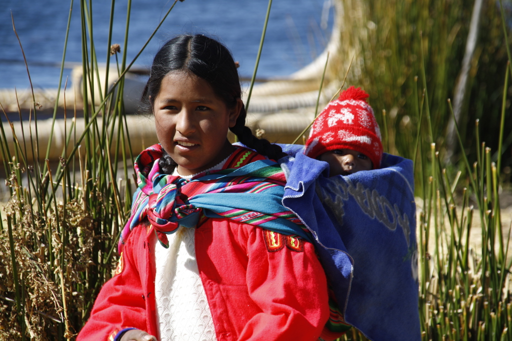 Vrouw draagt baby op haar rug bij het Titicacameer, Peru.