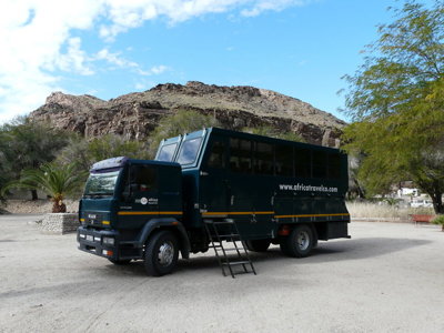 Donkergroene safari truck voor een truck-en-tent rondreis in Zuidelijk Afrika, geparkeerd bij rotsachtig landschap.