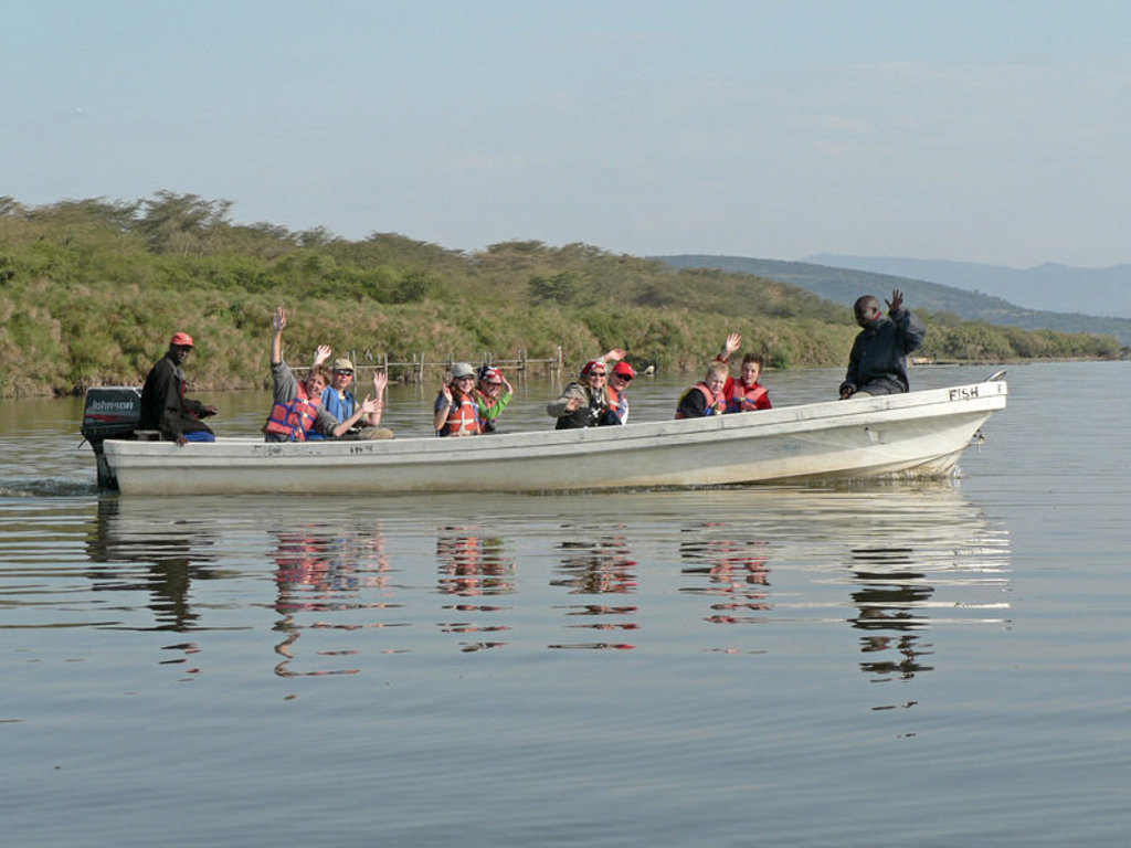 Groepsrondreis Kenia en Tanzania: reizigers in reddingsvesten zwaaien vanaf een boot op een meer.