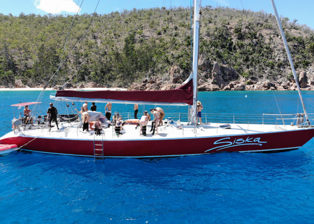 Zeilboot met reizigers in helderblauw water langs een rotsachtige kust tijdens een 22-35ers reis Australië.
