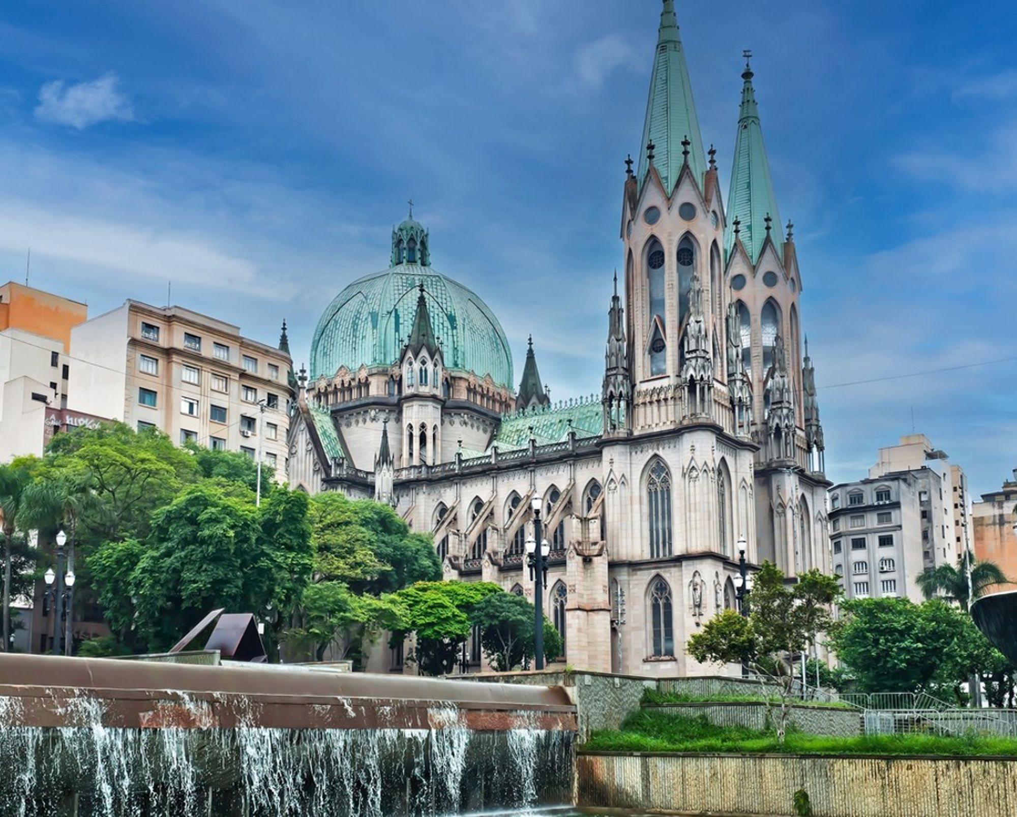 Kathedraal van São Paulo met groene koepel en torenspitsen, gezien vanaf het plein met fontein.