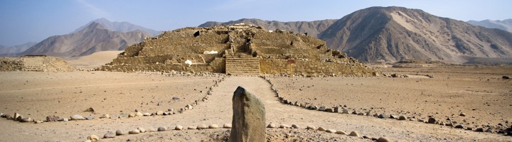 Ruïnes van Caral in Peru met stenen platform en ceremoniële monoliet in de woestijn.