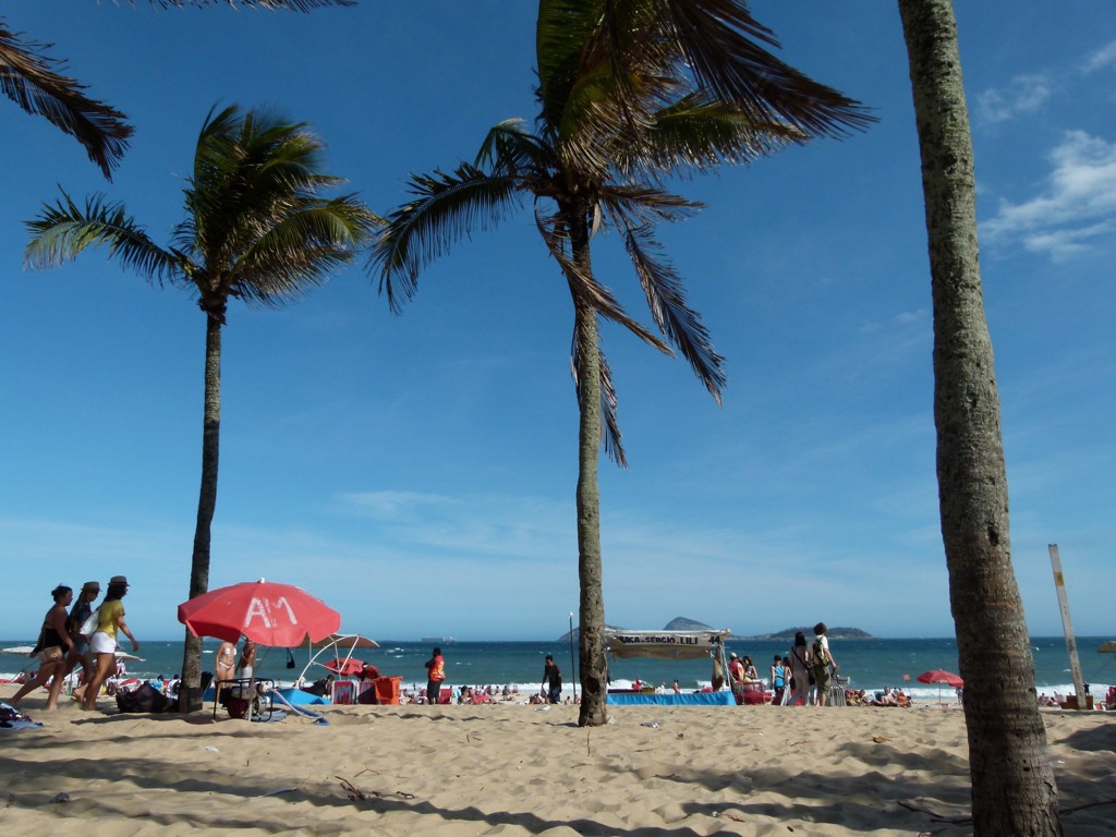 Zandstrand in Brazilië met palmbomen, strandgangers en parasols aan zee.