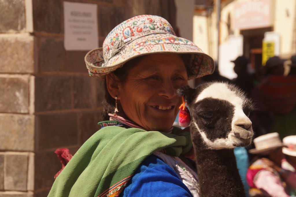 Vrouw met kleurrijke hoed houdt een jonge alpaca vast tijdens familiereis Peru.