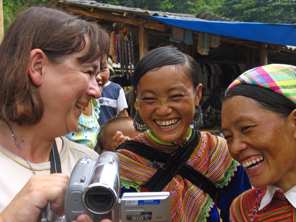 Reizigers lachen met lokale vrouwen in kleurrijke kleding op een markt tijdens groepsrondreis Vietnam.