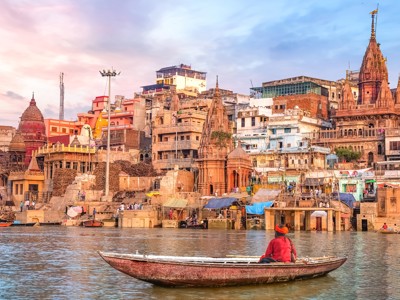 Boot op de Ganges bij de ghats van Varanasi, met tempels en kleurrijke gebouwen langs de rivier.