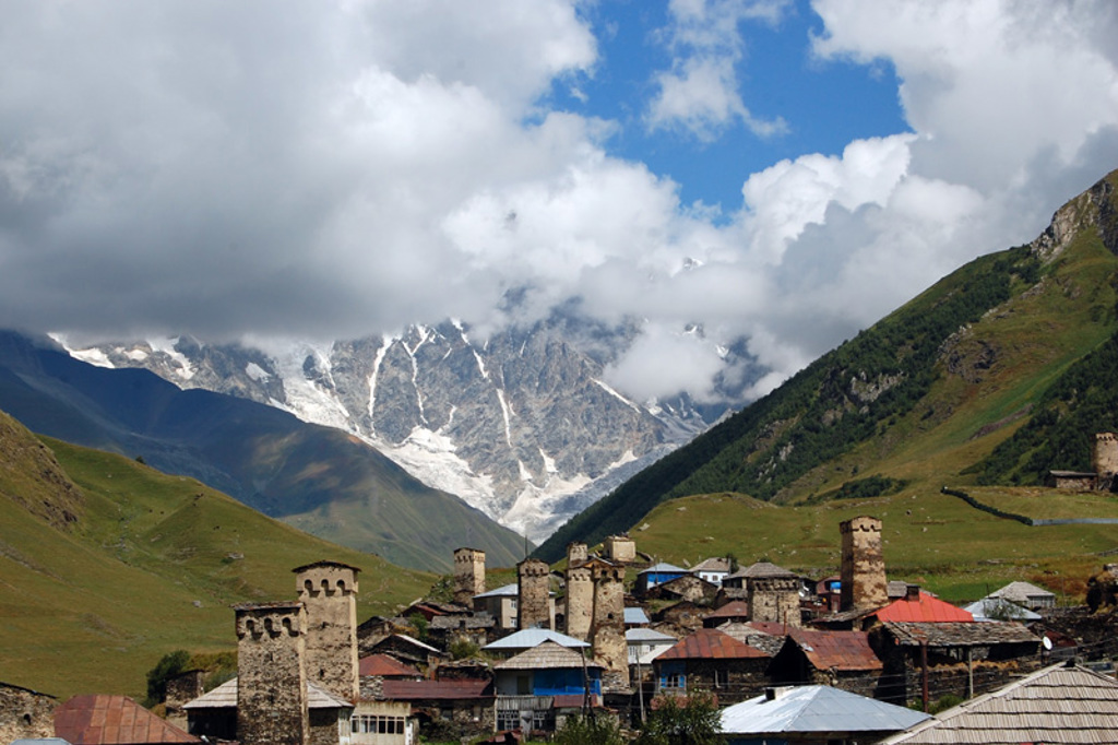 Bergdorp in Georgië met middeleeuwse verdedigingstorens en besneeuwde Kaukasuspieken op de achtergrond.