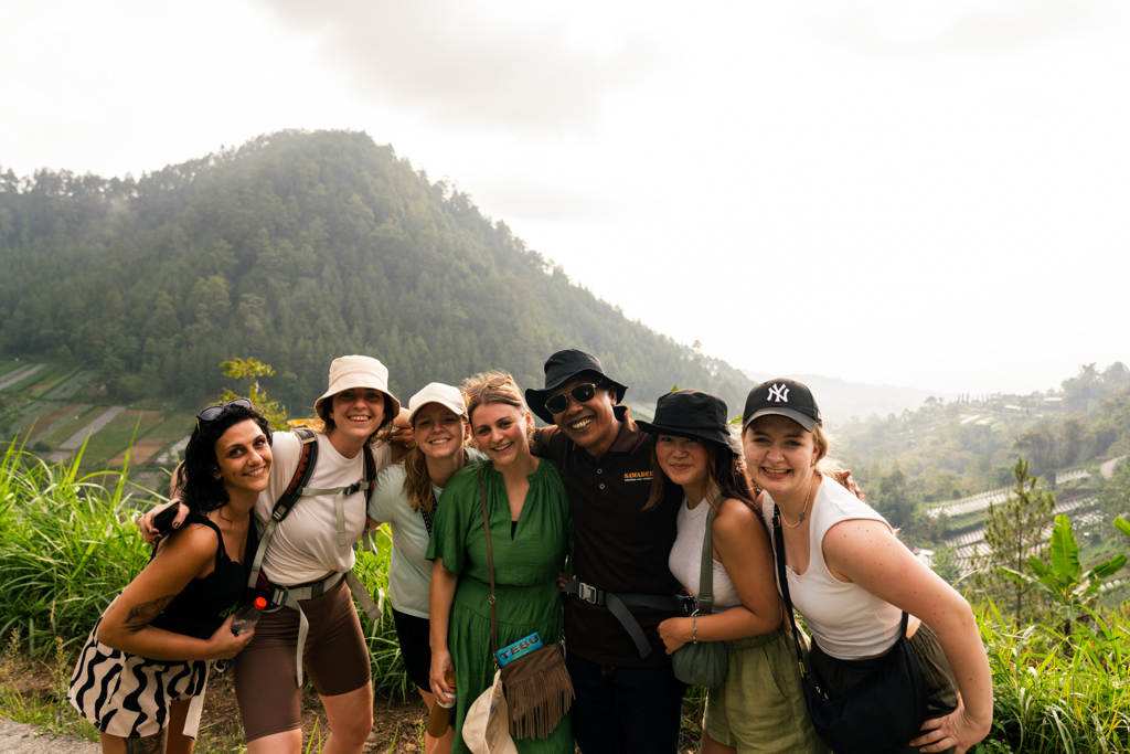 Groep 22-35ers reizigers poseert met gids tijdens rondreis op Java en Bali, met groene bergen op de achtergrond.