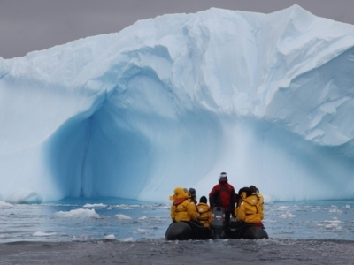 Zodiacboot met reizigers vaart langs een enorme ijsberg in Antarctica tijdens de Route Antarctica.