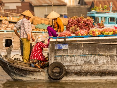 Drijvende markt in Vietnam met boten vol fruit en handelaren met conische hoeden.