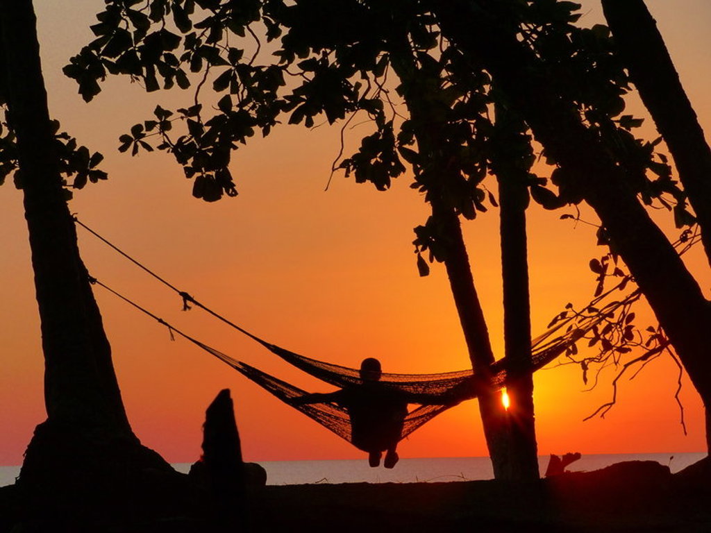 Silhouet van reiziger in hangmat tussen bomen bij zonsondergang aan de kust van Costa Rica.