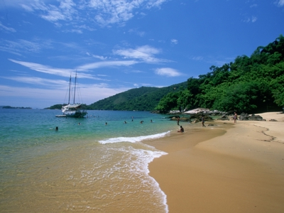 Strand bij Ilha Grande met zeilboot voor anker en groen beboste heuvels, op de route van Buenos Aires naar Rio.