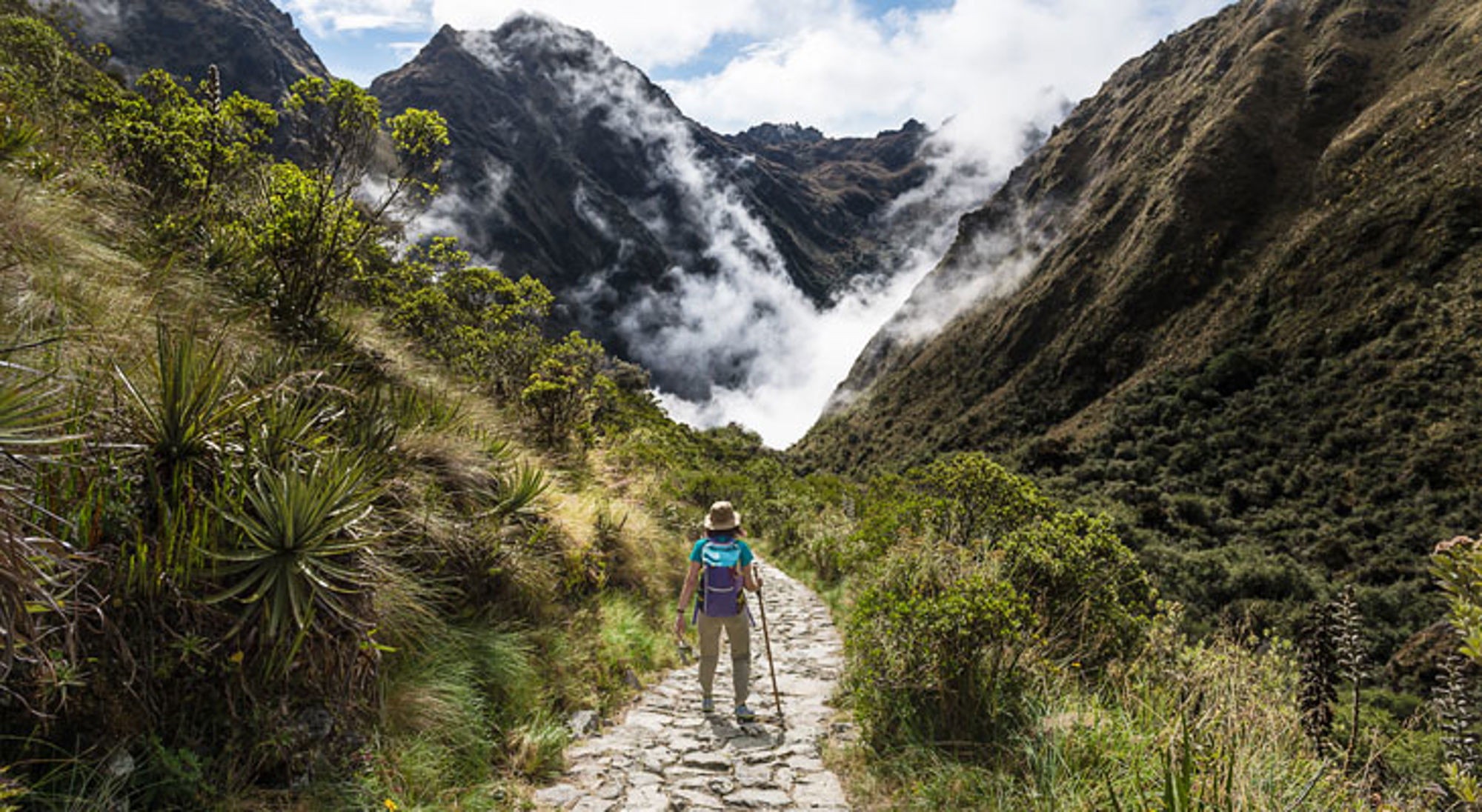 Wandelaar op bergpad in de Peruaanse Andes met mistige valleien en hoge bergtoppen.