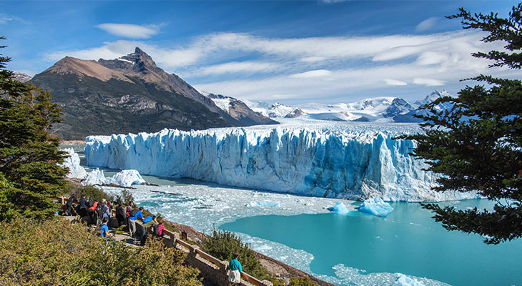 Uitzicht op de Perito Moreno-gletsjer in Patagonië, met bezoekers op het uitkijkpunt en bergen op de achtergrond.