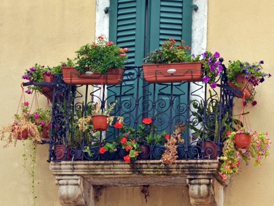 Balkon met smeedijzeren hekwerk, groene luiken en bloembakken vol kleurrijke bloemen tijdens de Route Balkan.