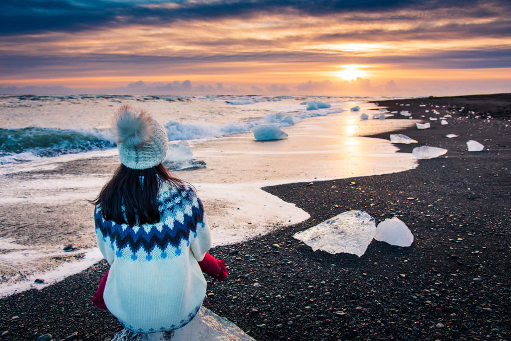 Reiziger op zwart strand met ijsbrokken bij zonsondergang in IJsland tijdens 22-35ers groepsrondreis.