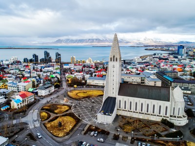 Hallgrímskirkja-kerk in Reykjavik met kleurrijke huizen, baai en besneeuwde bergen op de achtergrond.