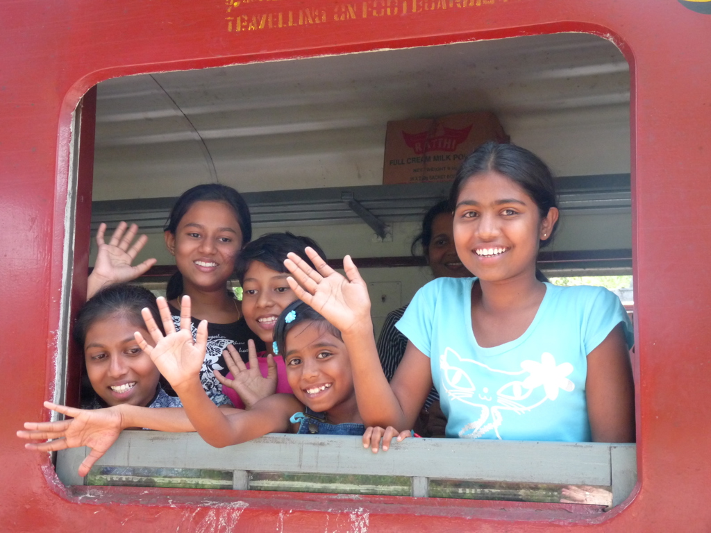 Vrolijke kinderen zwaaien vanuit het raam van een rode trein in Sri Lanka.