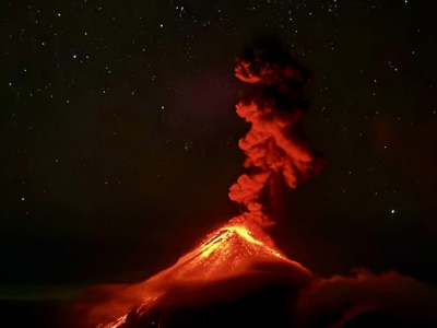 Uitbarstende vulkaan in Guatemala met gloeiende lava en aswolk onder een heldere sterrenhemel.