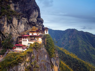 Tijgernestklooster (Paro Taktsang) tegen een steile rotswand in Bhutan, met uitzicht over beboste Himalayavallei.