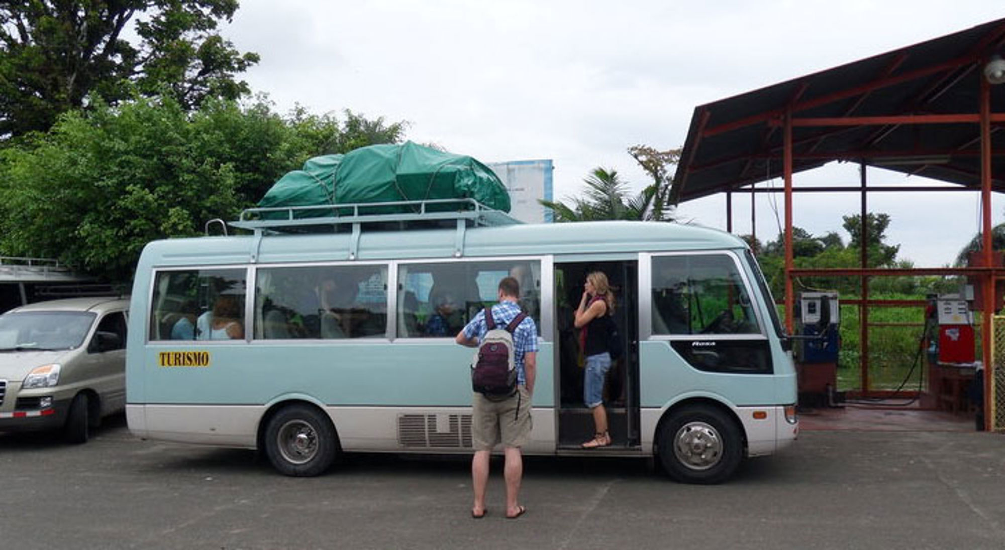 Toeristen stappen in een minibus met bagage op het dak bij een tankstation in Costa Rica.