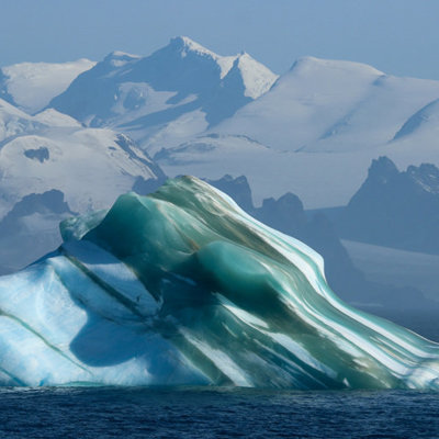 Drijvende ijsberg voor besneeuwde bergen in Antarctica tijdens een groepsrondreis per boot.
