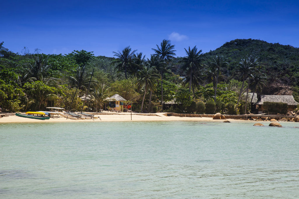 Tropisch strand in Vietnam met palmbomen, helderblauw water en vissersbootjes langs de kust.
